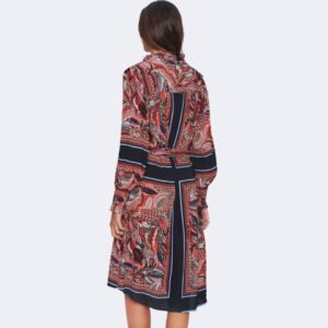 Η πίσω όψη του μακρυμάνικου εμπριμέ φορέματος σε κόκκινους και μπλε τόνους. Η γυναίκα στέκεται όρθια με τα χέρια χαλαρά στο πλάι. Διακρίνονται οι κάθετες και οριζόντιες γραμμές του μοτίβου, η πλάτη με το συνεχόμενο σχέδιο και το μήκος που φτάνει κάτω από το γόνατο. Φόντο καθαρό, ανοιχτό γκρι.