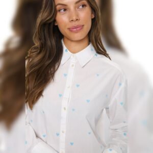 Γυναίκα με μακριά καστανά μαλλιά φοράει λευκό πουκάμισο με μικρές γαλάζιες καρδιές, κοιτάζοντας στο πλάι.