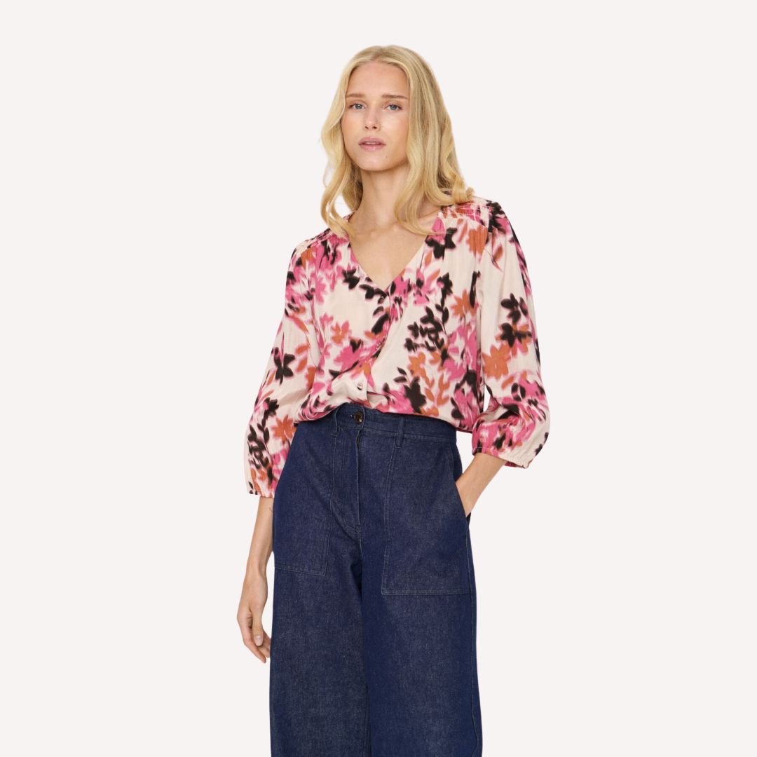 Μοντέλο φοράει γυναικεία φλοράλ μπλούζα με V λαιμόκοψη και τζιν παντελόνι σε casual chic look.