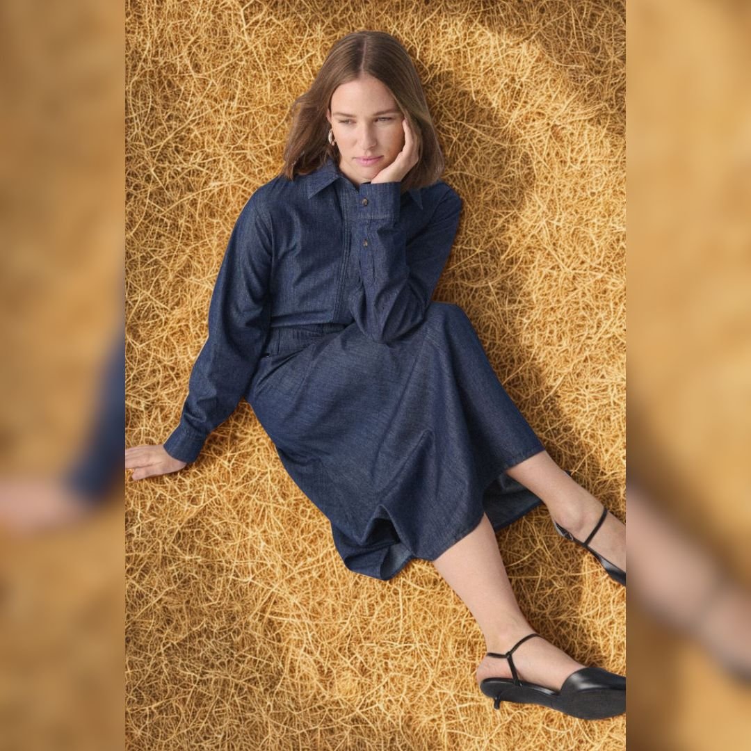 1-30408497 «Γυναίκα μεσαίου ύψους κάθεται σε χρυσαφένιο φόντο φορώντας σκούρο μπλε denim πουκαμισοφόρεμα με μακριά μανίκια και γιακά, δημιουργώντας φυσικό και χαλαρό look.»