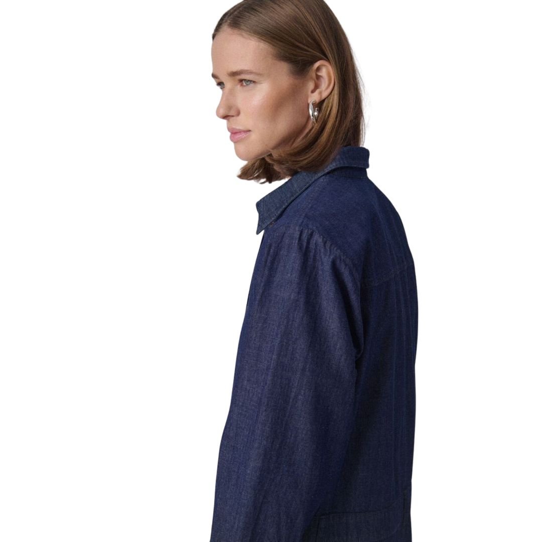 2-30408497 «Προφίλ γυναίκας που φορά denim πουκαμισοφόρεμα σε dark indigo χρώμα, με καθαρή ραφή και απλό γιακά, σε ουδέτερο φόντο.»