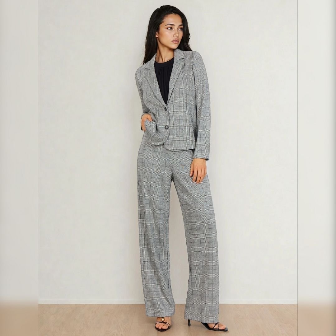 «Γυναικείο σετ με καρό σακάκι και παντελόνι σε γκρι αποχρώσεις τύπου Prince of Wales. Το μοντέλο φορά το σακάκι κουμπωμένο με ένα κουμπί και το συνδυάζει με μαύρη μπλούζα και μαύρα πέδιλα. Το ύφασμα είναι μαλακό με ελαφριά ελαστικότητα και το φόντο είναι ουδέτερο εκρού, σε ξύλινο δάπεδο.»
