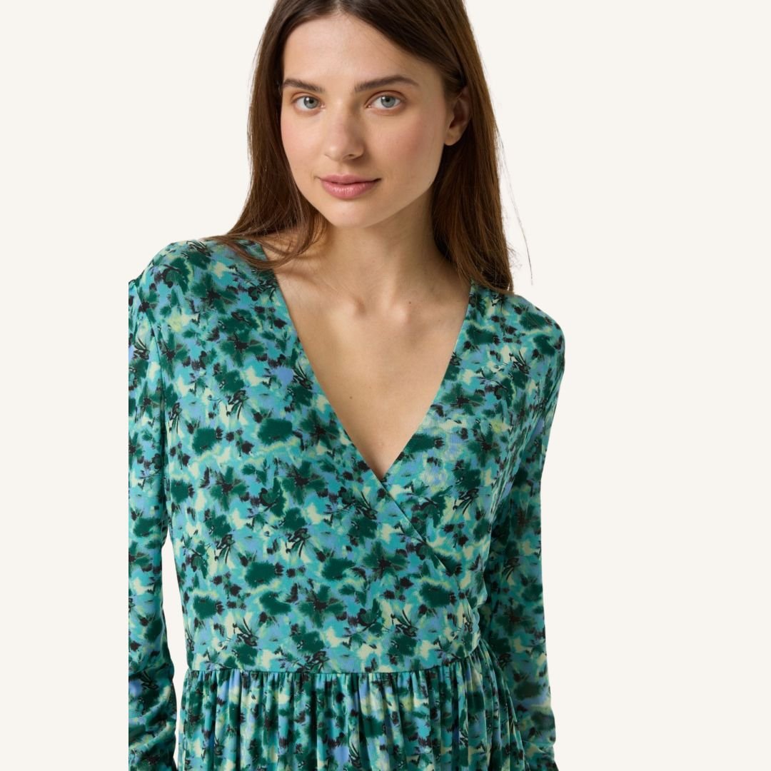 4-30407727 Κοντινό πορτραίτο γυναίκας που φορά πράσινο μίντι φόρεμα με λουλουδάτο μοτίβο. Διακρίνεται το V ντεκολτέ, η απαλή υφή του υφάσματος και οι λεπτομέρειες του σχεδίου, σε λευκό φόντο