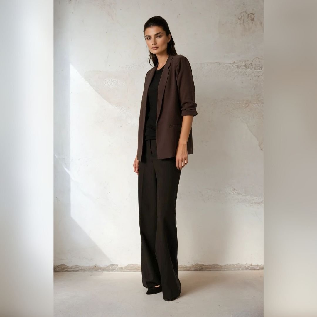 «Μοντέλο ποζάρει με σοκολατί καφέ blazer Soaked in Luxury, μαύρη μπλούζα και μαύρο wide-leg παντελόνι. Φόντο σε ανοιχτό, textured τοίχο με φυσικό φως για soft, minimal αισθητική.»