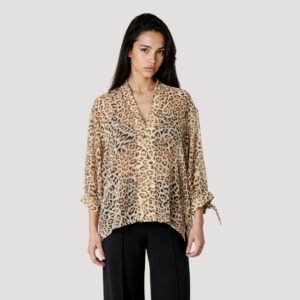 «Γυναίκα φοράει ημιδιάφανη λεοπάρ μπλούζα Soaked in Luxury με χαλαρή εφαρμογή, V ντεκολτέ και μανίκια 3/4 με δεσίματα. Συνδυασμένη με μαύρο παντελόνι. Ουδέτερο ανοιχτό φόντο.»