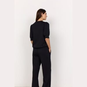 Όψη από πίσω μοντέλου που φοράει μαύρη μπλούζα με φουσκωτά μανίκια μέχρι τον αγκώνα, με καθαρό minimal φόντο.