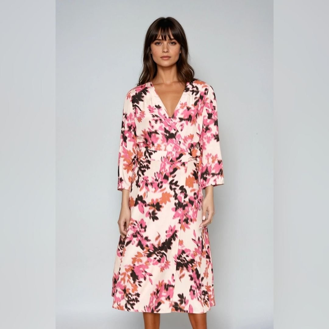 «Γυναίκα μοντέλο φοράει midi κρουαζέ φόρεμα σε εκρού βάση με έντονο floral μοτίβο σε ροζ, κοραλί και μαύρες αποχρώσεις. Το φόρεμα δένει στη μέση και έχει μανίκια 3/4. Το μοντέλο στέκεται σε ουδέτερο, ανοιχτό γκρι φόντο, με φυσικό φωτισμό.»
