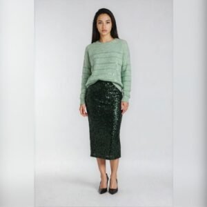Mint πλεκτό πουλόβερ με χαλαρή εφαρμογή και διακριτικές ριγέ λεπτομέρειες με ελαφριά λάμψη, συνδυασμένο με πράσινη midi παγιέτα φούστα και μαύρες γόβες, φορεμένο σε ουδέτερο ανοιχτό φόντο.