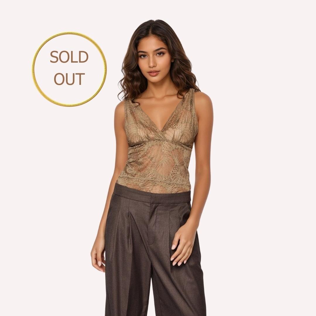 Γυναικείο δαντελένιο τοπ σε μπεζ-χρυσή απόχρωση, με αμάνικο σχέδιο και V ντεκολτέ, εφαρμοστή γραμμή και διακριτική διαφάνεια. Το μοντέλο το φορά με καφέ υφασμάτινο παντελόνι. Στην εικόνα υπάρχει ένδειξη “Sold Out”.