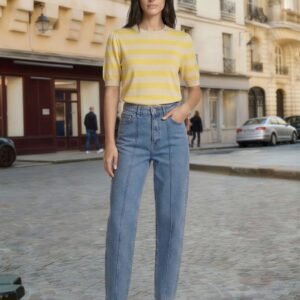 Γυναικεία καλοκαιρινή εμφάνιση με ριγέ κοντομάνικη μπλούζα σε απαλές αποχρώσεις κίτρινου και μπεζ, με ίσια εφαρμογή και στρογγυλή λαιμόκοψη. Συνδυάζεται με ψηλόμεσο τζιν παντελόνι σε ίσια γραμμή και λευκά sneakers για casual chic αποτέλεσμα. Το look αποτυπώνεται σε αστικό φόντο με ευρωπαϊκή αρχιτεκτονική, προσδίδοντας κομψή, καθημερινή αισθητική.