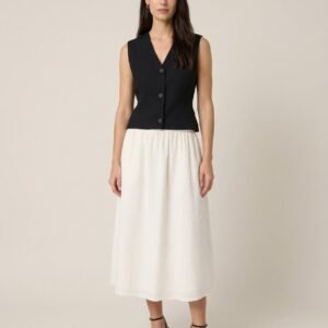 Γυναικεία μίντι φούστα σε εκρού απόχρωση με ανάγλυφη υφή και ελαστική μέση, σε χαλαρή γραμμή, συνδυασμένη με μαύρο αμάνικο τοπ και πέδιλα με τακούνι, σε ουδέτερο studio φόντο.