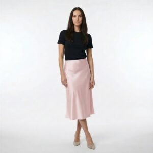 Γυναίκα φορά μίντι σατέν φούστα σε ροζ πούδρα με απαλή, ρευστή υφή και ελαφρώς Α-line εφαρμογή, συνδυασμένη με μαύρο fitted t-shirt και μυτερές γόβες, σε καθαρό λευκό studio φόντο.