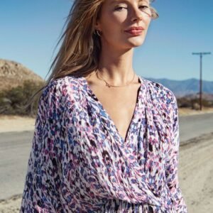 Κοντινή λήψη από μίντι κρουαζέ φόρεμα με abstract print σε ροζ και γαλάζιες αποχρώσεις, με ανάλαφρο ύφασμα, ντραπέ λαιμόκοψη και φαρδιά μανίκια, φορεμένο από μοντέλο σε ηλιόλουστο εξωτερικό τοπίο.