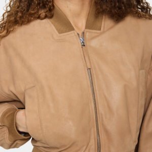 Λεπτομέρεια γυναικείου bomber jacket σε καμηλό σουέντ υφή με μεταλλικό φερμουάρ και ριπ γιακά, minimal αισθητική σε καθαρό φόντο