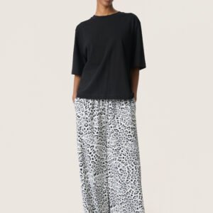 Wide leg παντελόνα με ασπρόμαυρο leopard print συνδυασμένη με μαύρο T-shirt και μοντέρνα γυαλιά ηλίου. Casual chic εμφάνιση σε μπεζ studio φόντο.