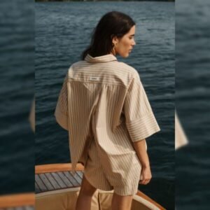 Γυναικείο μπεζ ριγέ σορτς Soaked in Luxury από ελαφρύ υφαντό ύφασμα με ελαστική μέση, φορεμένο με ασορτί πουκάμισο, πίσω όψη σε ξύλινο σκάφος με θαλάσσιο φόντο.